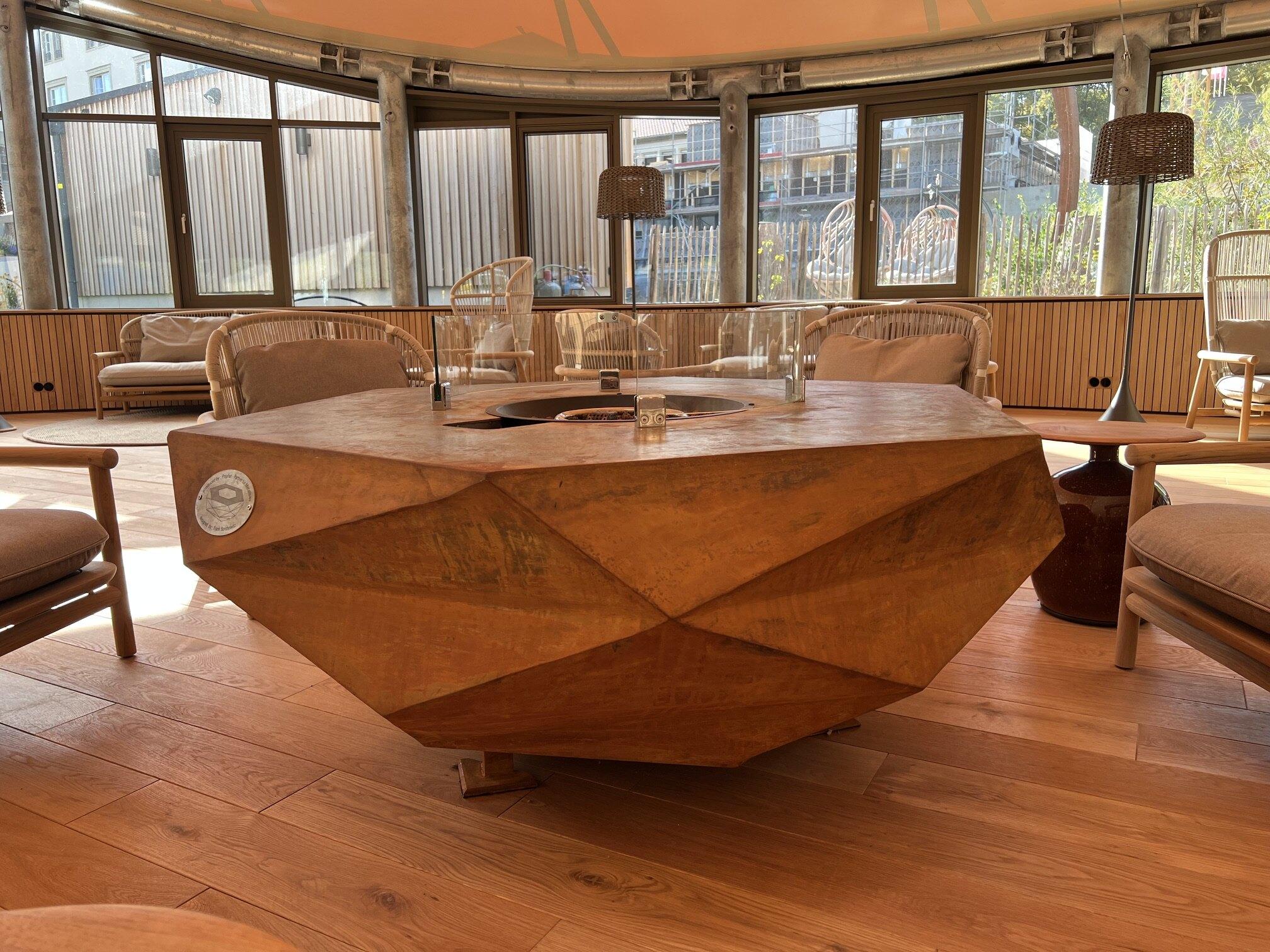 Gas-fired Iron Icon with glass wind guard, surrounded by lounge chairs in a glazed pavilion at Hotel Schindelbruch