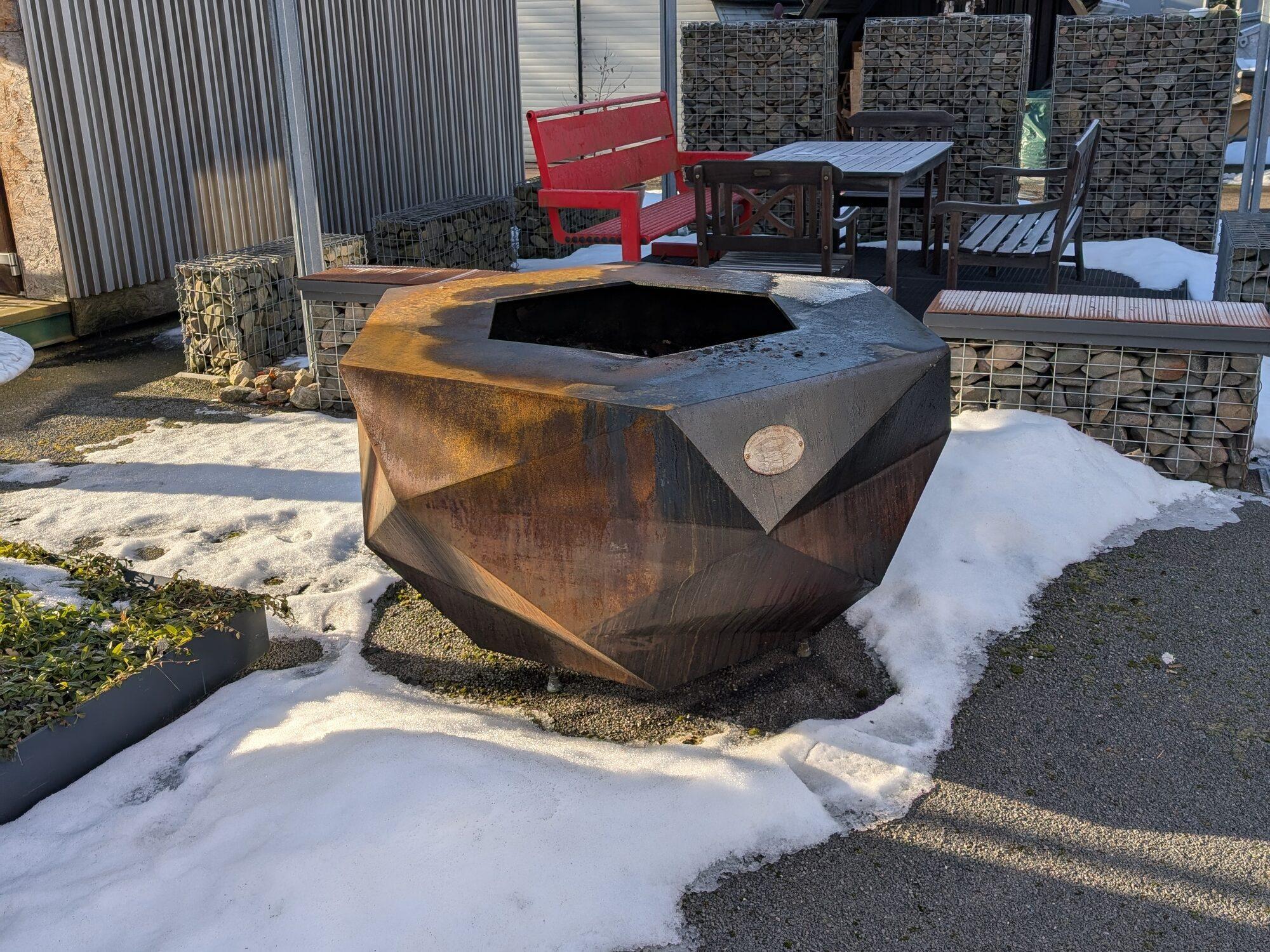 Corten fire bowl on a snow-covered terrace in winter light