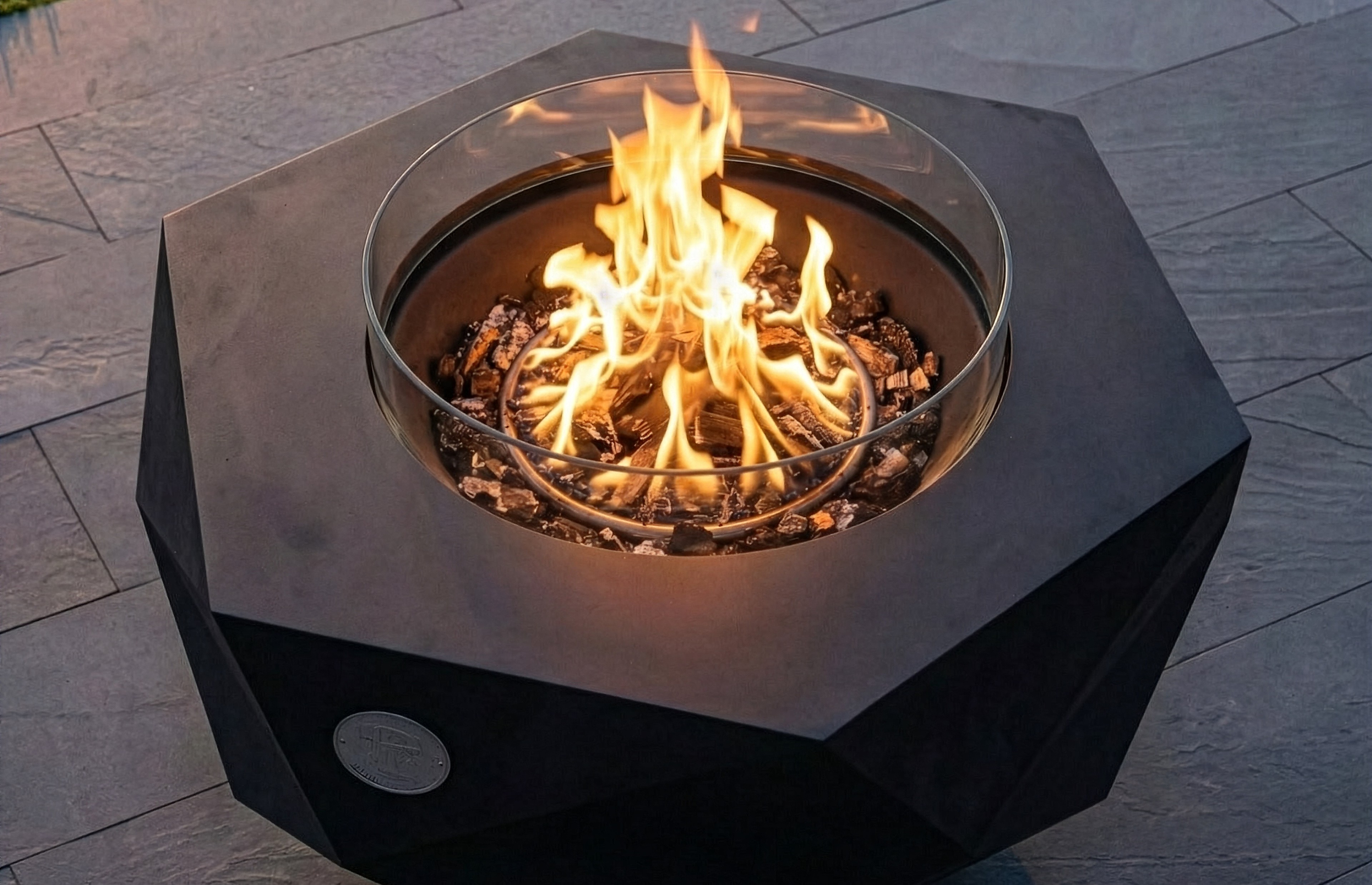 Fire burning behind the glass wind guard of an Iron Icon fire bowl on a stone terrace