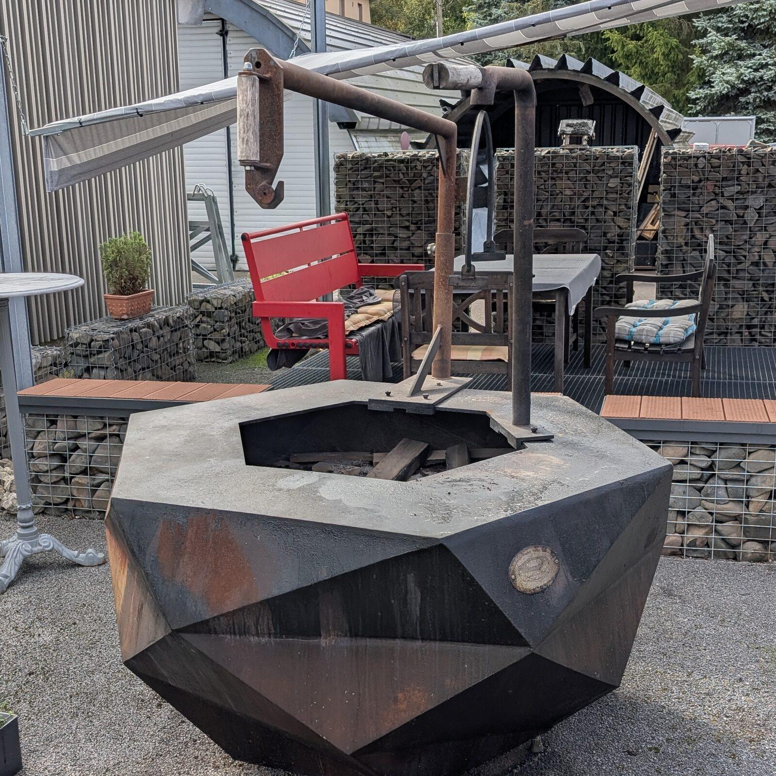 Fire bowl in the blackened finish with a swing arm mounted over the fire opening